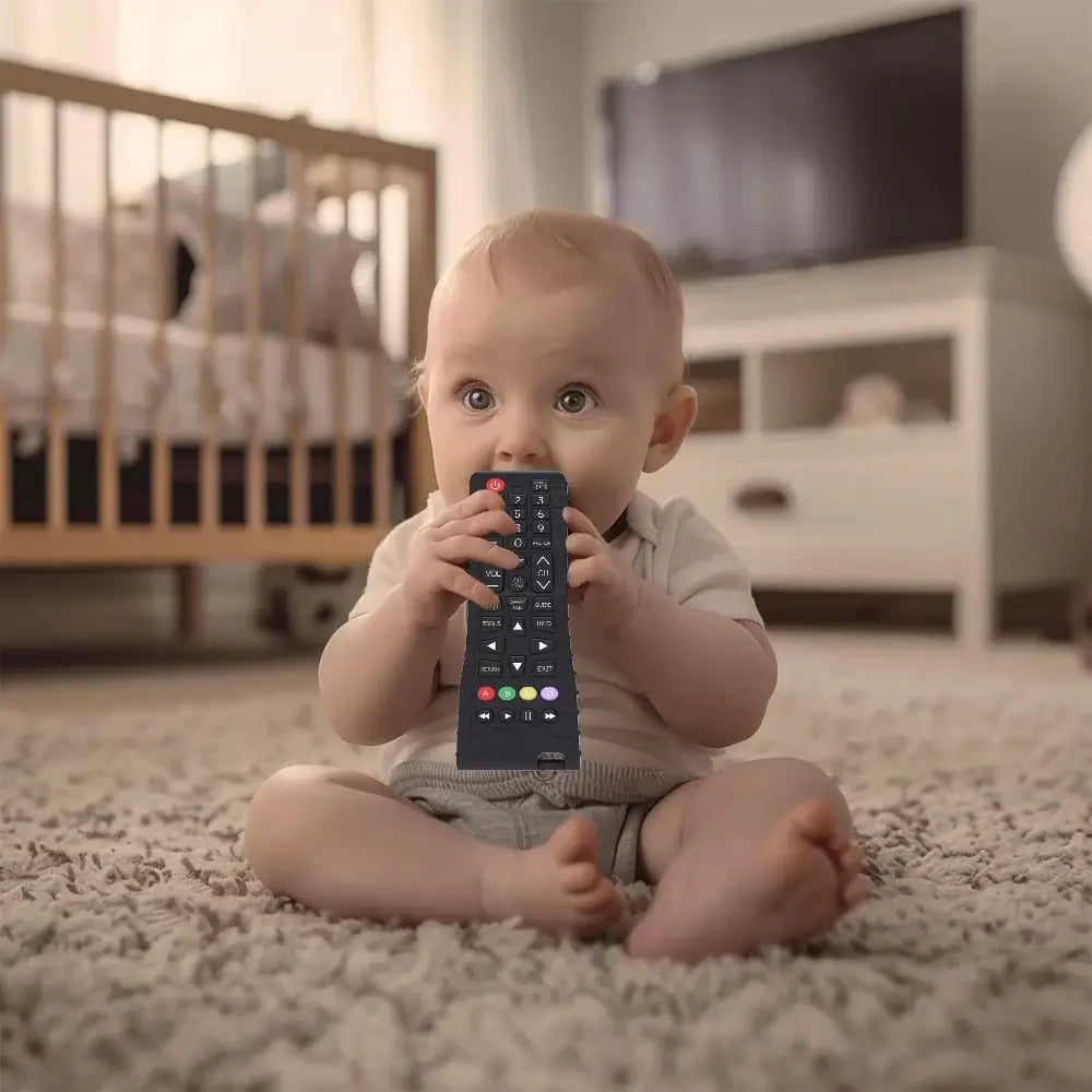 Baby sitting on carpet chewing a silicone teether toy shaped like a TV remote control.